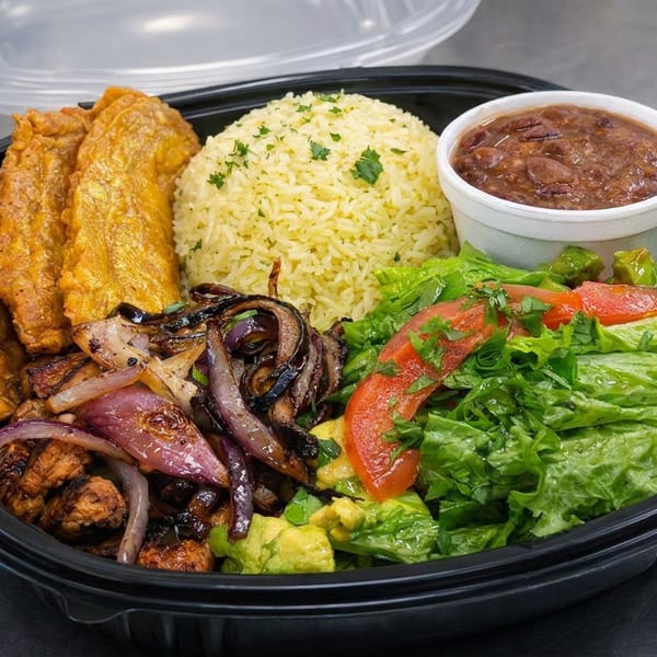 Takeout platter with fried plantains, seasoned rice, beans, grilled onions, avocado, lettuce, and tomato salad.